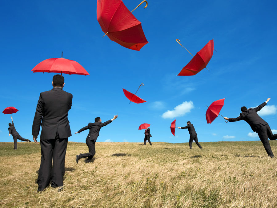 businessmen difficulty holding red umbrellas blown by wind