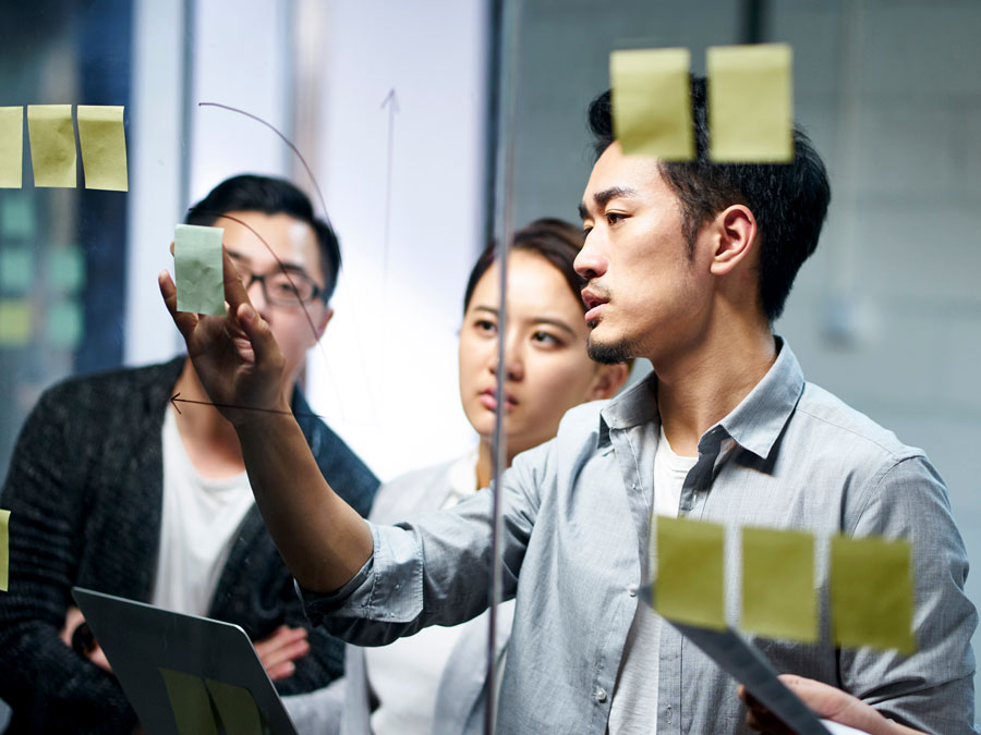 japanese call center team leader discussing business plans on glass postit notes