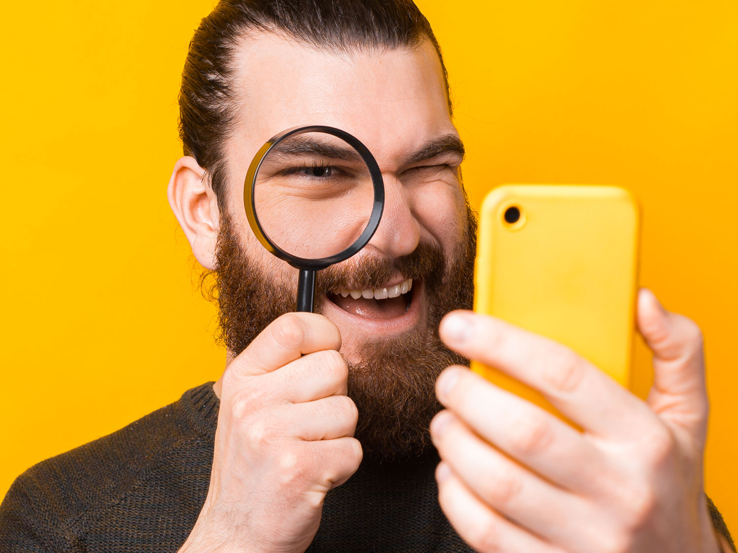 content moderation analyst looking at yellow smartphone with magnifying lens glass