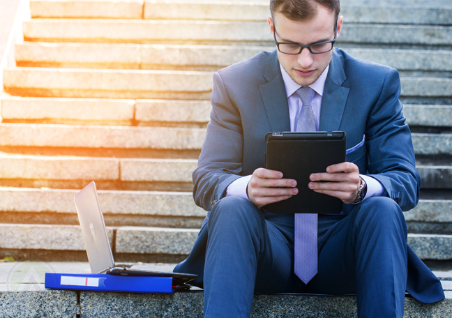 young businessman sitting on stone steps reading tablet