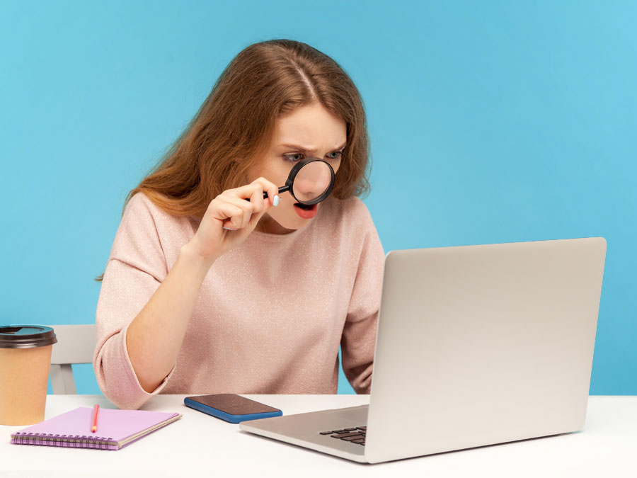 outsourced content moderation analyst looking at laptop through magnifying lens
