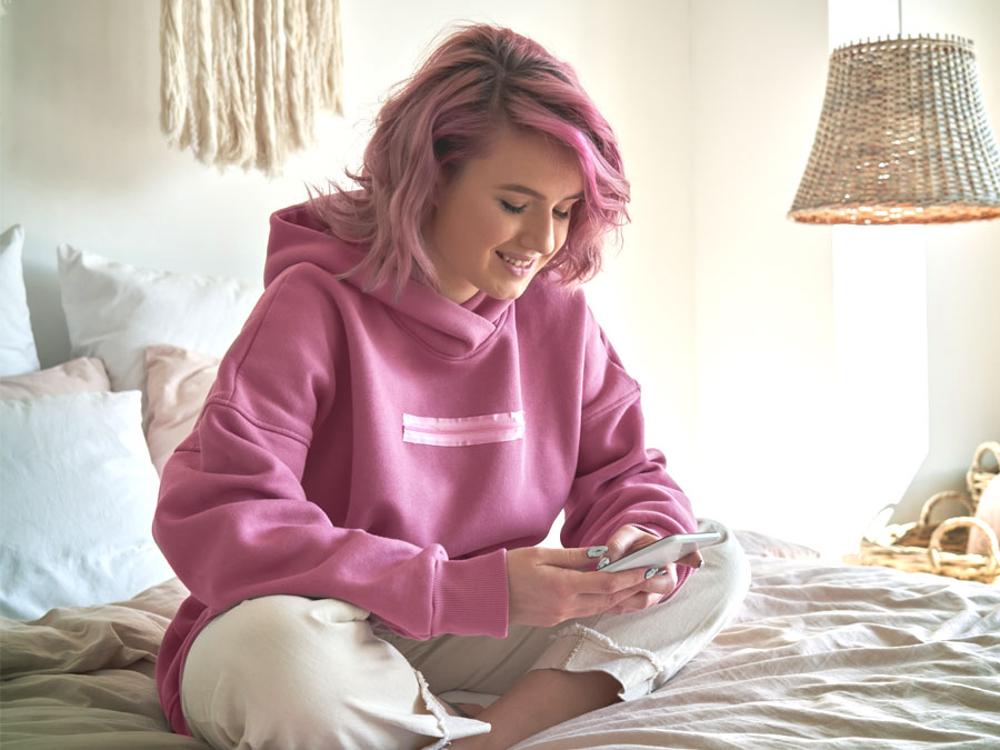 gen z girl pink hair using smartphone on bed
