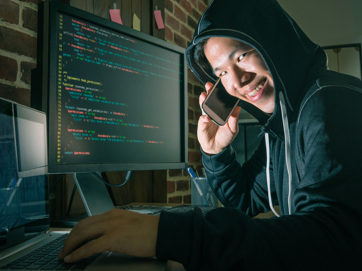 sneaky criminal in hood using telephone and computer