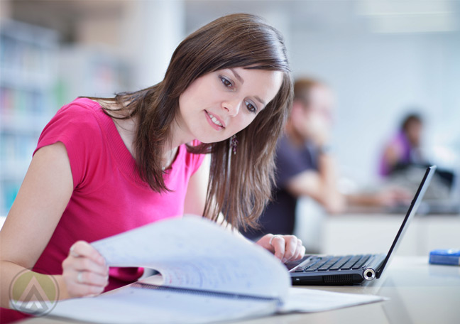 female-employee-in-pink-reading-from-paper-and-on-laptop