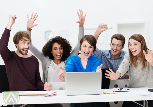 excited-diverse-millennial-employees-huddled-together-over-a-laptop