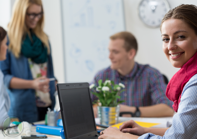 smiling-female-employee-on-laptop-with-chatting-coworkers