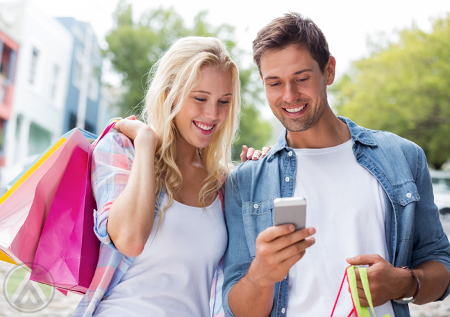 female-male-couple-with-shopping-bags-smiling-over-smartphone