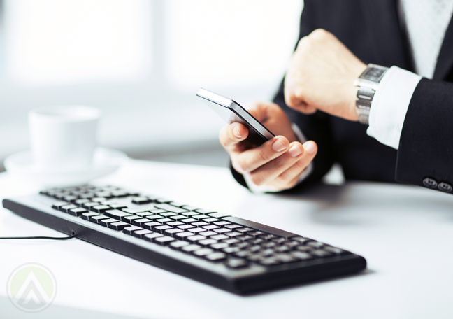 businessman-using-computer-holding-smartphone-looking-at-watch