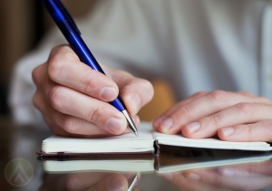 close-up-hand-holding-ball-point-pen-writing-on-notebook