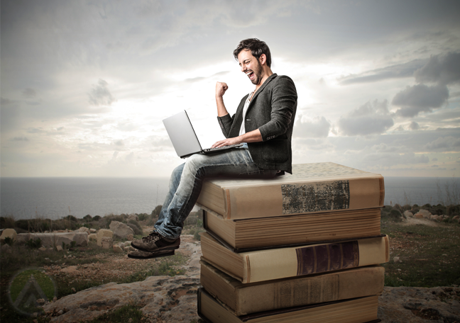 excited-man-using-laptop-sitting-on-stack-of-giant-book-in-desert