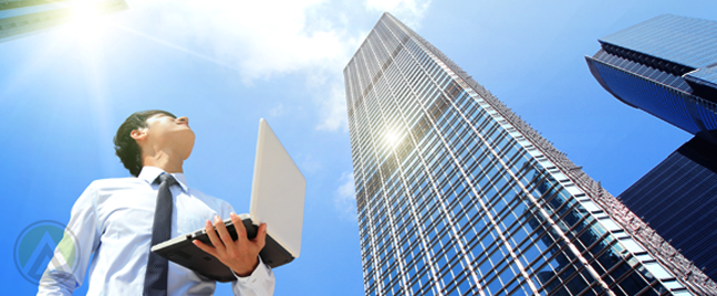 young-asian-male-businessman-holding-laptop-outdoors-looking-up-at-building