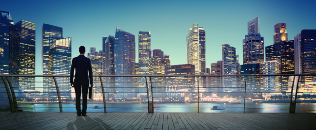 businessman-standing-on-building-balcony-looking-over-cityscape-after-sunset