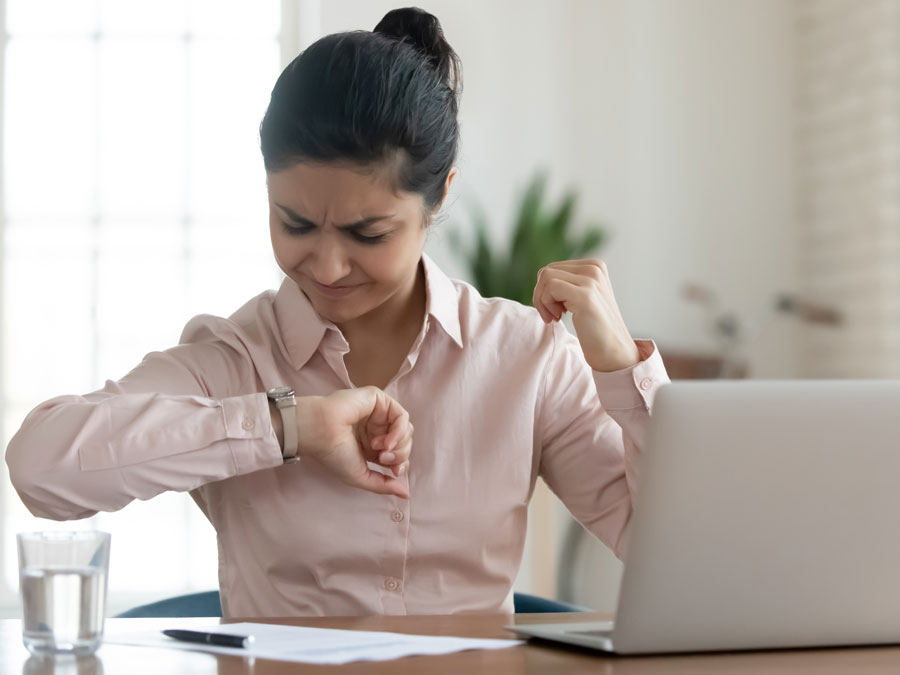 stressed woman using laptop looking at wrist watch