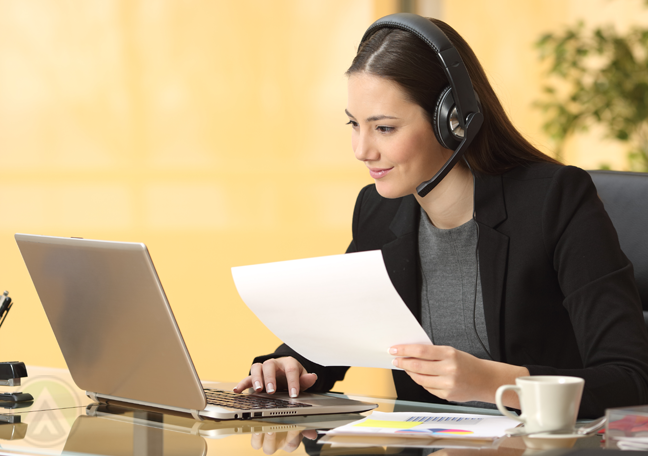 smiling-customer-service-call-center-agent-using-laptop-holding-printed-document