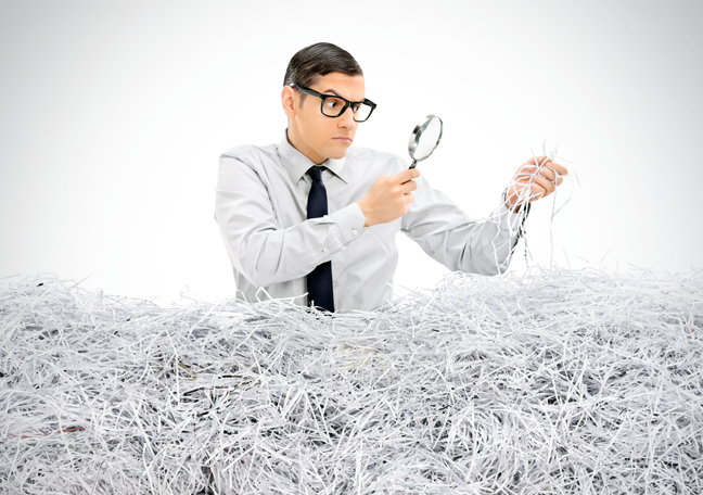 dorky-business-employee-by-piles-of-shredded-paper-looking-through-magnifying-lens