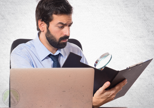 bearded office worker looking at folder of reports with magnifying lens