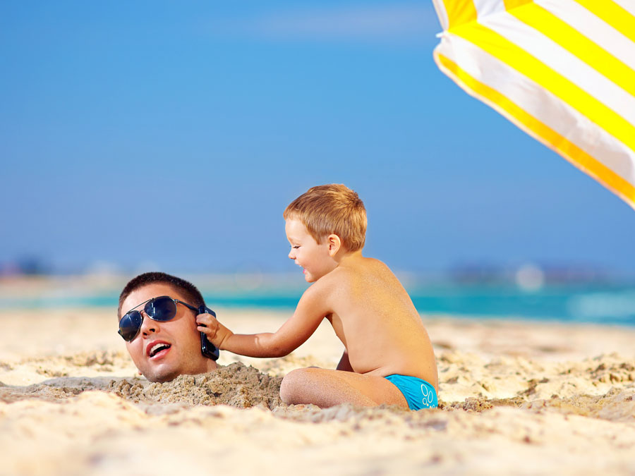 father and son in beach using phone under yellow umbrella