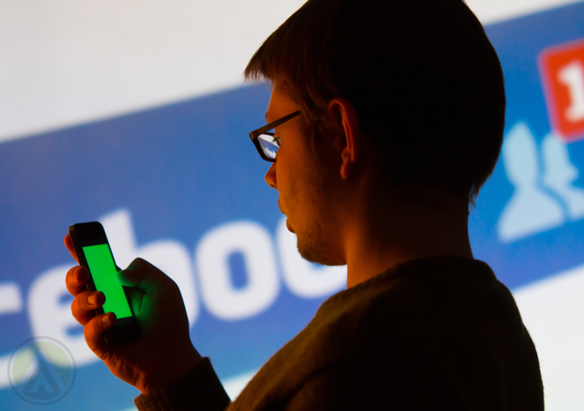 man in glasses reading smartphone by Facebook logo