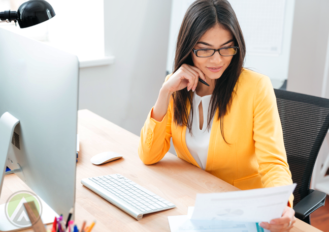 businesswoman reading printed report by computer in office