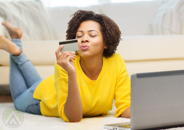 womani n yellow lying on floor using laptop kissing credit card