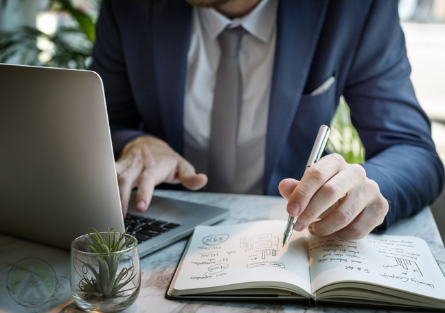 businessman using laptop writing on notebook with pen