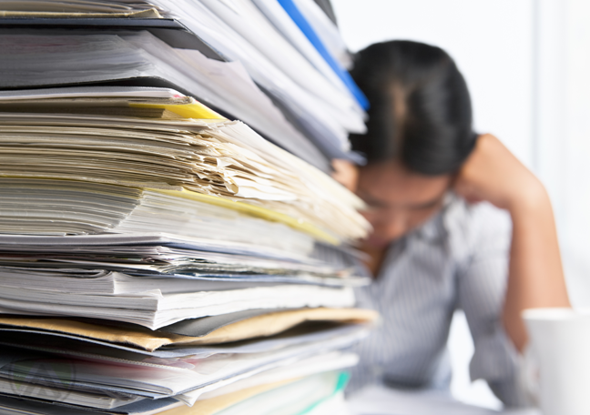 employee reading behind large pile of printed paperwork research reports