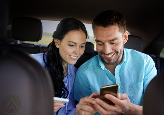 happy couple using smartphone in back of car