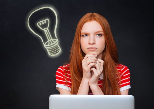 red head woman using laptop thinking by chalkboard with light bulb drawing