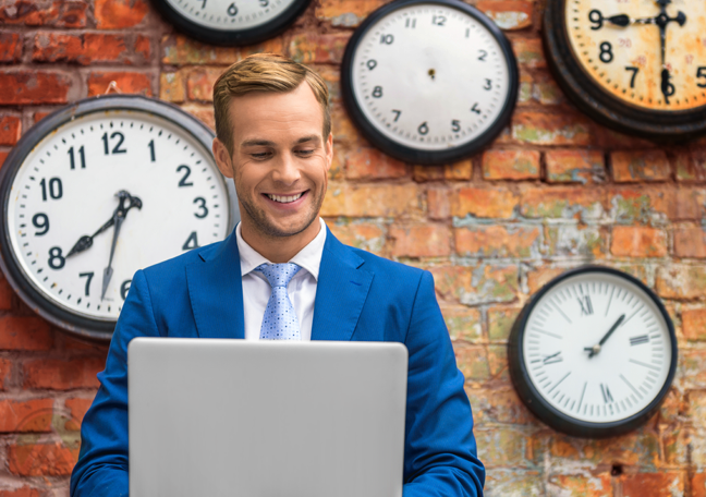 smiling businessman in blue suit by red brick wall with wall clocks