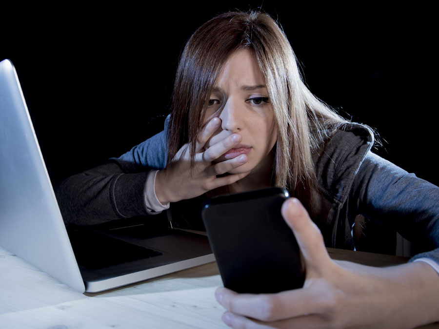 problematic employee by laptop in dark looking at smartphone