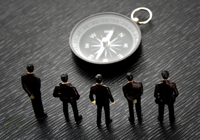 tiny human figures standing before compass