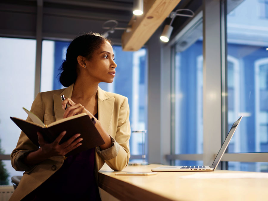 content creator thinking of customer service looking out window holding notebook with laptop