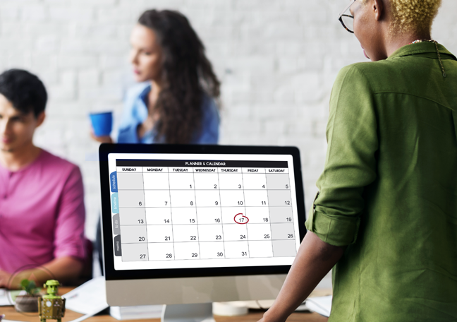 employee looking at calendar on computer coworkers in office 