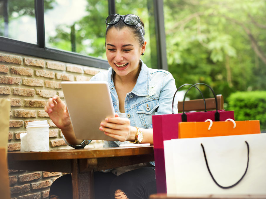 happy woman online shopping on tablet at cafe with shopping bags