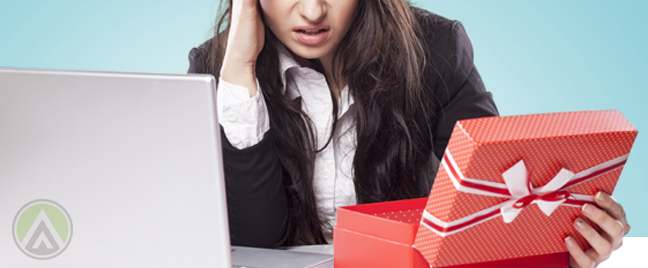 problematic female call center agent sitting by laptop looking at red opened gift box