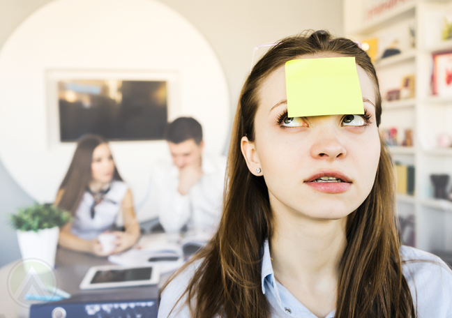 confused office employee with post it on forehead coworkers in back