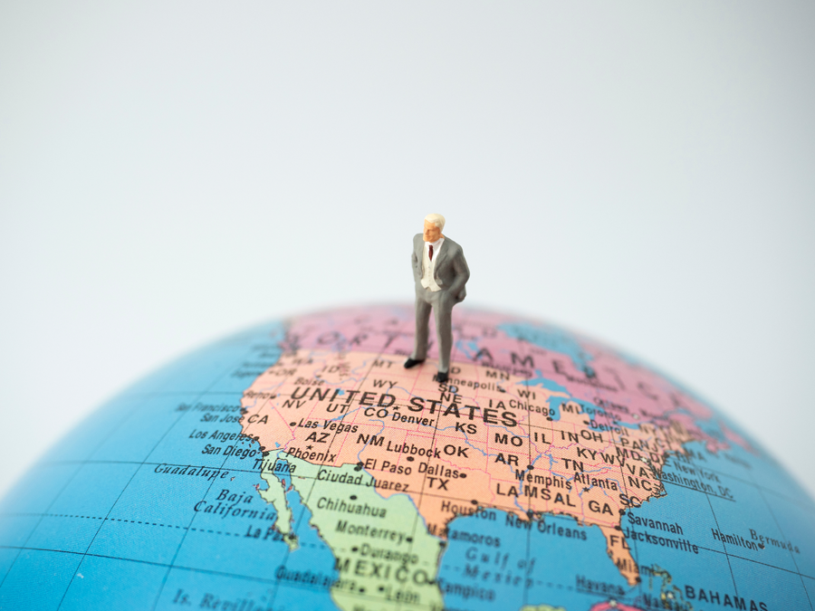 lone miniature businessman standing on top of globe