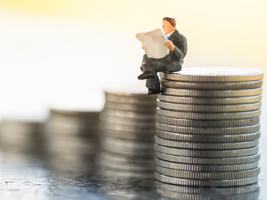 miniature executive reading newspaper on stack of coins showing business progress