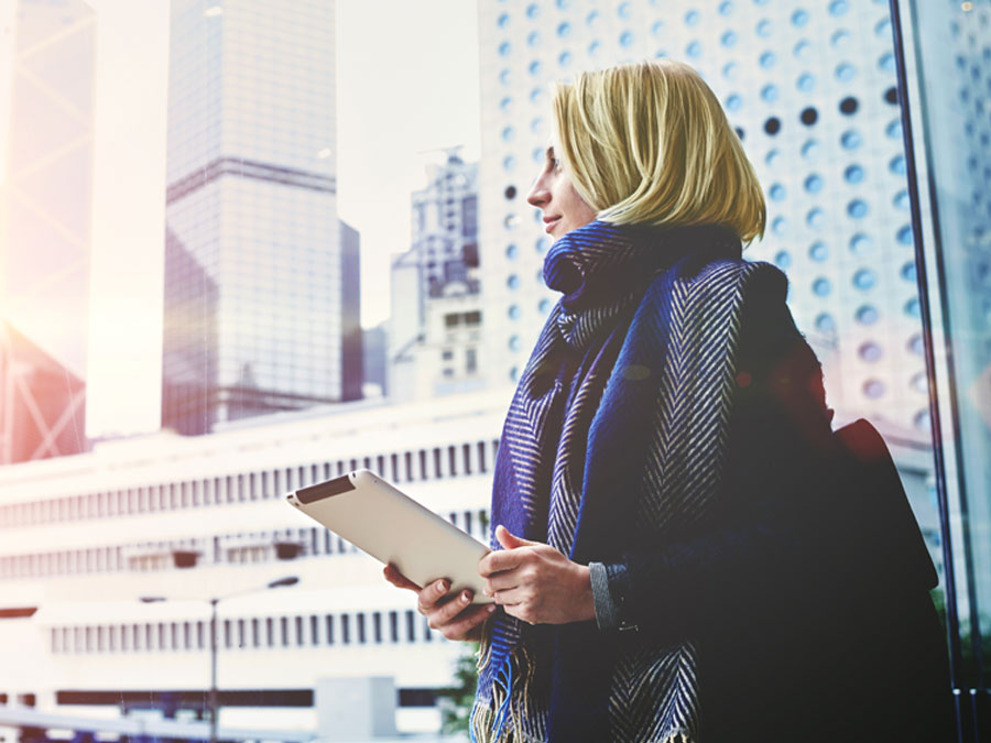 woman holding tablet looking out to buildings in the distance