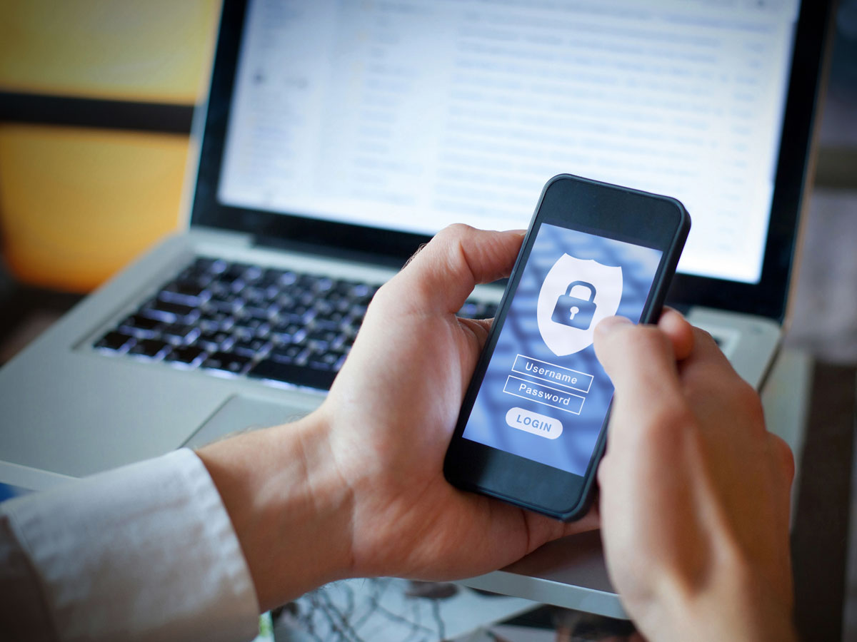 male hands using smartphone showing data security with laptop behind