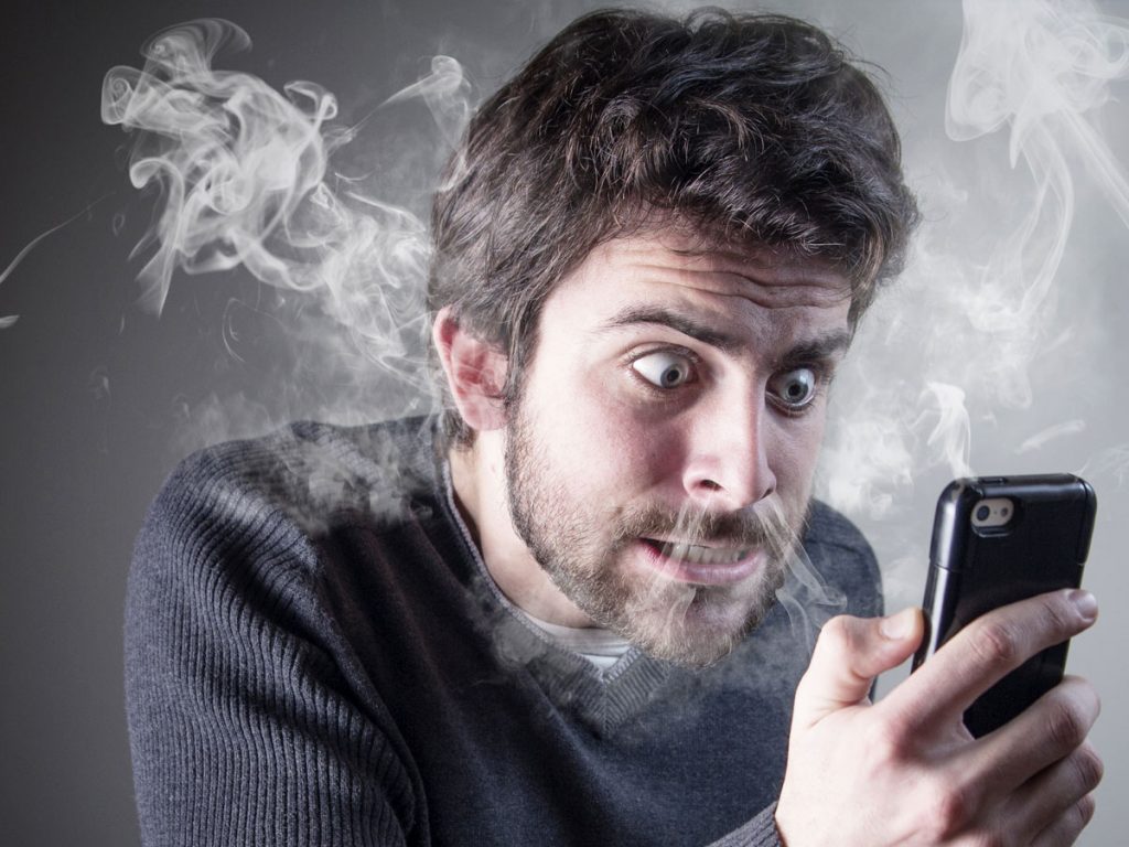 frustrated young man staring at phone as smoke blows from nose