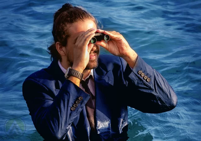 bearded-long-haired-businessman-in-the-ocean-lookign-through-binoculars