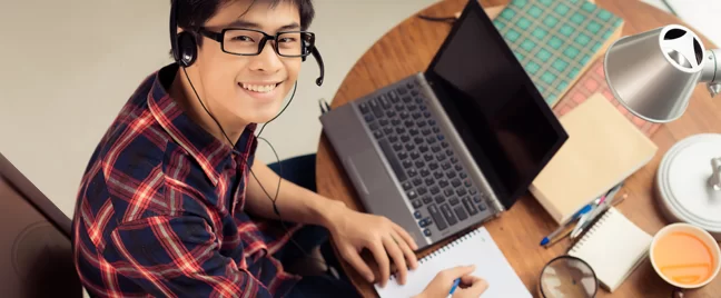 smiling-Asian-blogger-in-glasses-in-front-of-laptop-writing-on-notebook