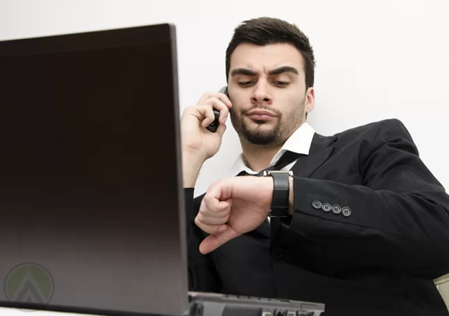 annoyed-businessman-in-phone-call-looking-at-watch-waiting-by-laptop