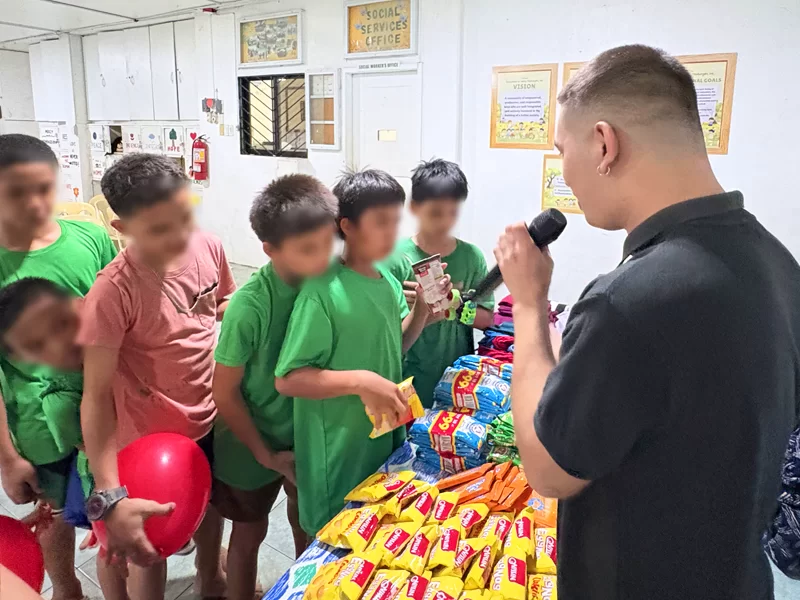 Community outreach programs by Open Access featuring a volunteer speaking with children as they receive snacks and care packages during a community outreach event.